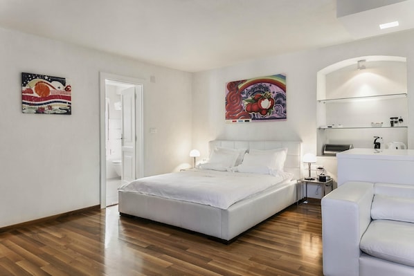 A modern bedroom with a large bed, a bedside table, a chair, and a bathroom with a mirror and shelves.