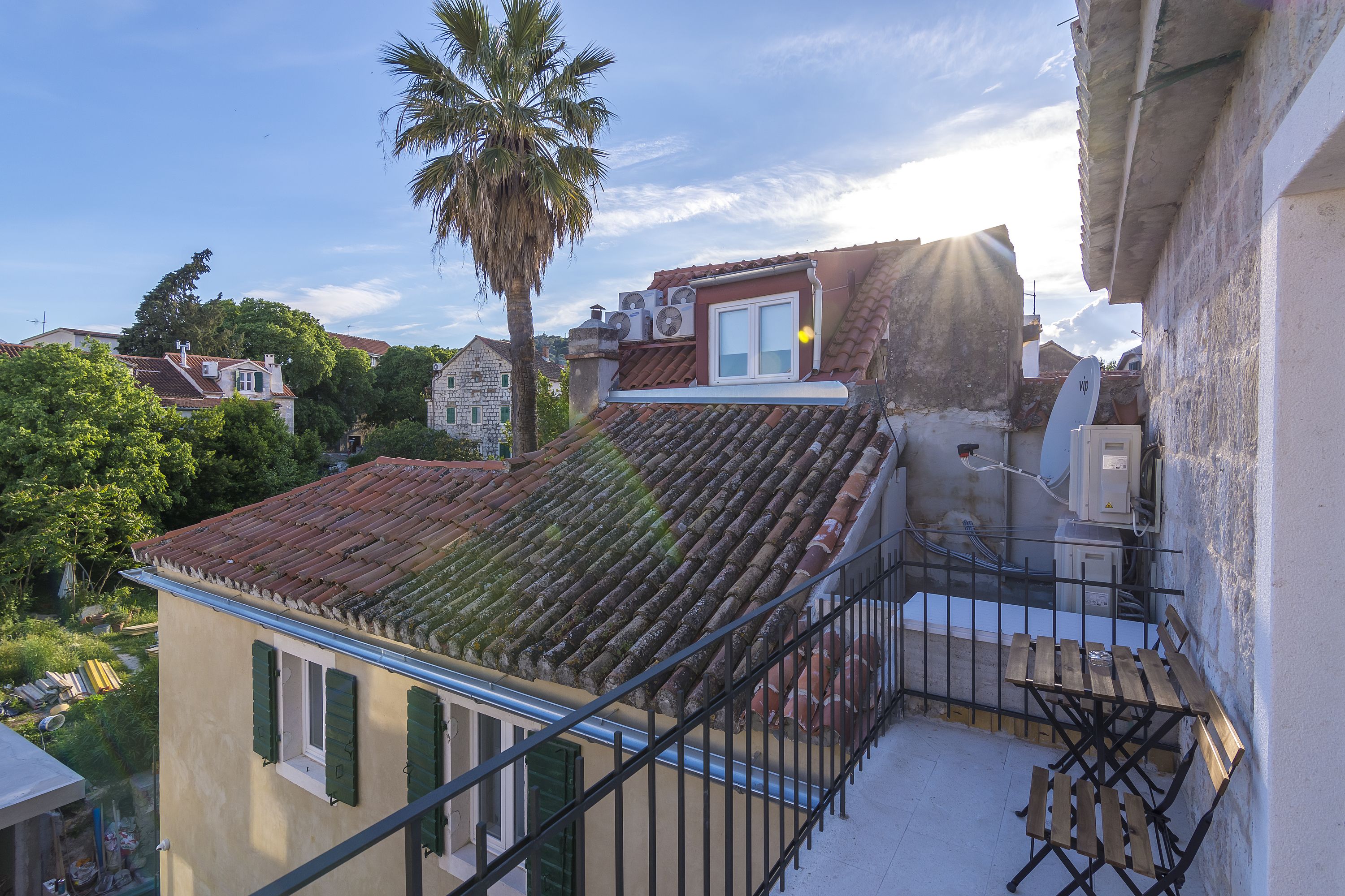Een balkon met uitzicht op omliggende gebouwen, een palmboom en een schotelantenne.