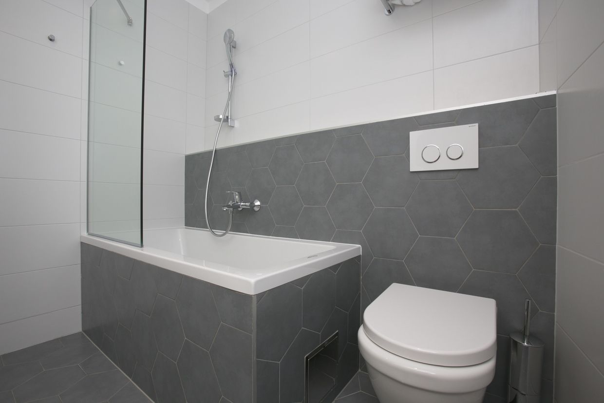 A modern bathroom with a glass-enclosed shower, a white bathtub, and a toilet.