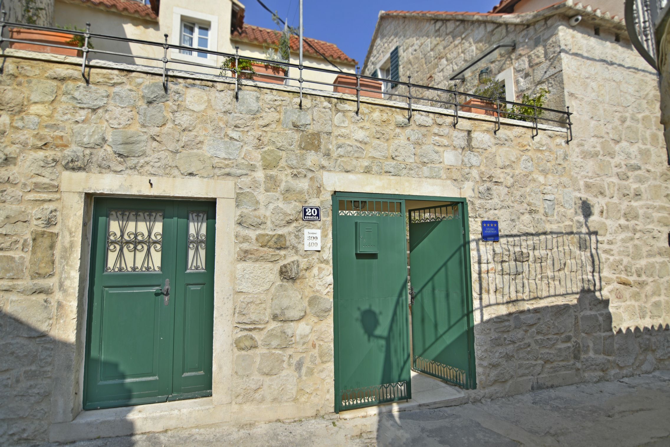 A stone building with two green doors, one with a metal gate and a sign indicating a 20-minute walk to the nearest bus stop.