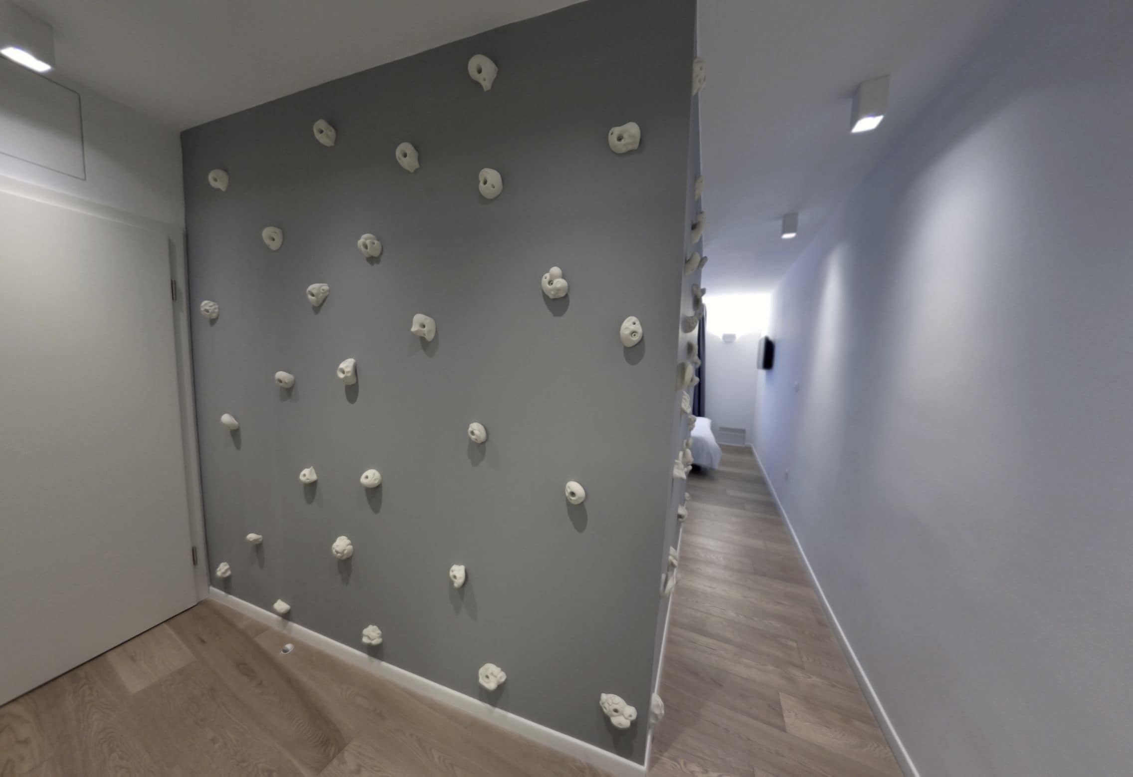 Ein Korridor mit einer grauen Wand, die mit Klettergriffen versehen ist, und einem Holzboden.