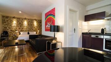 A modern living room with a stone wall, a black sofa, a glass coffee table, and a painting of a rainbow and tiger.