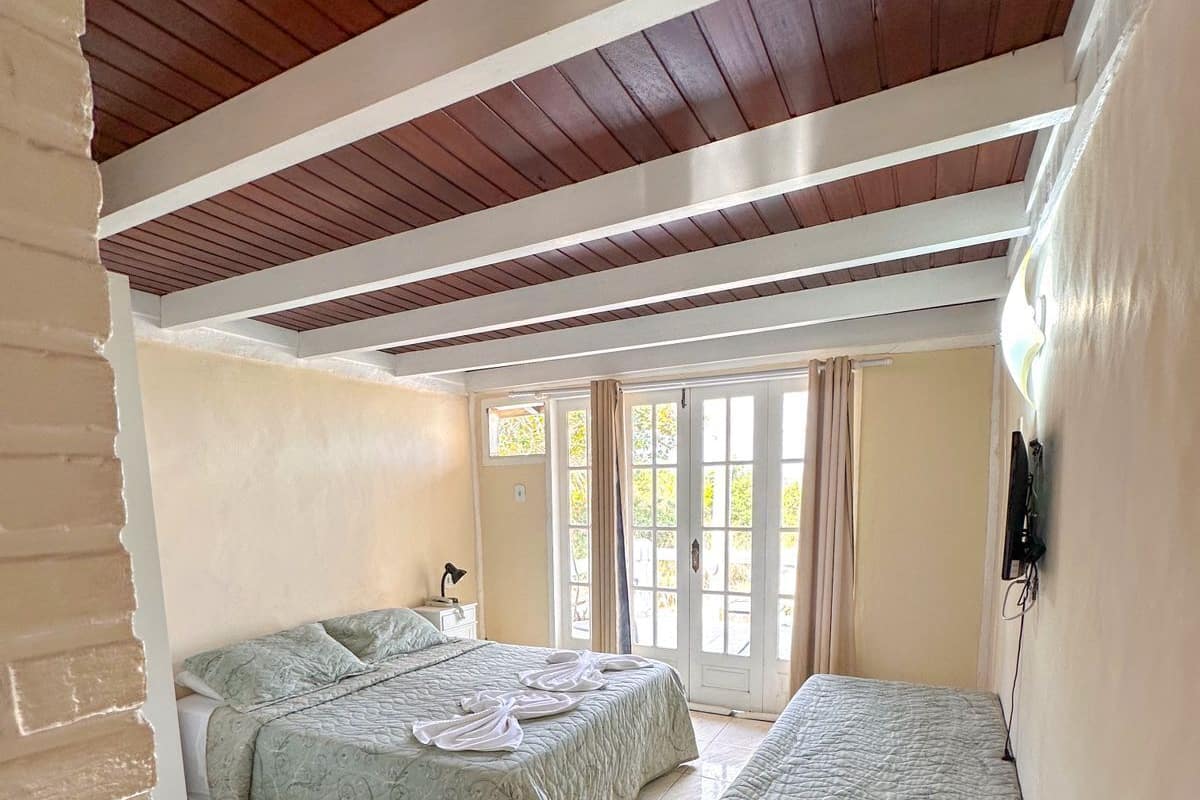 Ein Zimmer mit zwei Betten, einer Bank und einem großen Fenster mit Vorhängen.