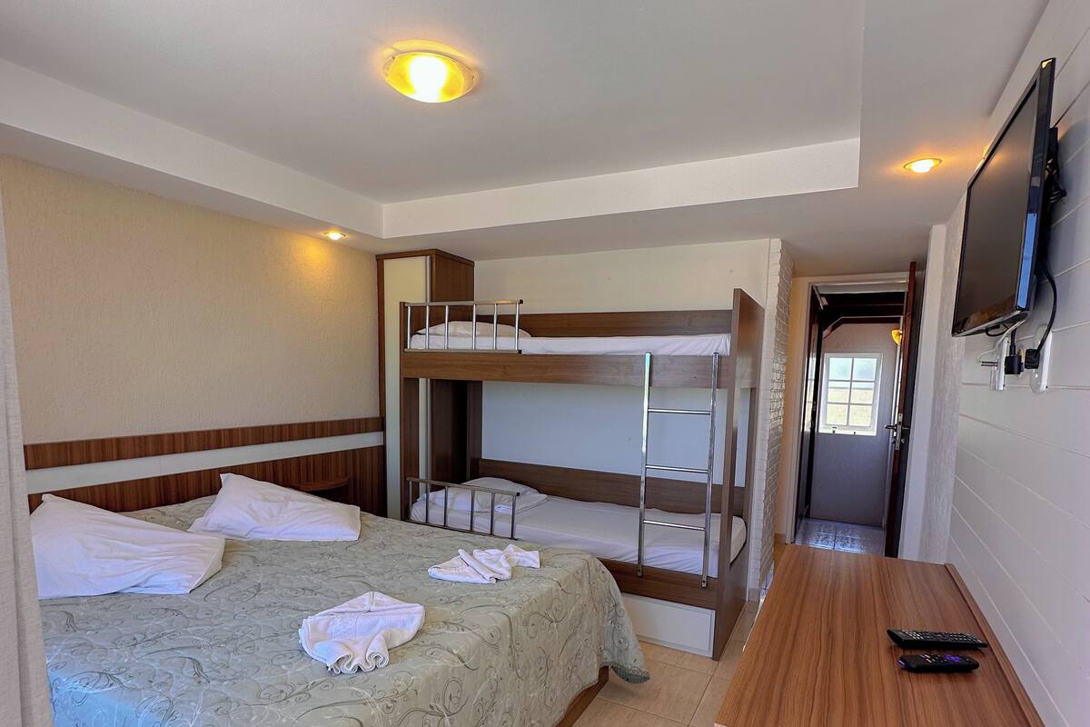 Ein Hotelzimmer mit Etagenbett, Schreibtisch, Fernseher und einem durch eine geöffnete Tür einsehbaren Badezimmer.