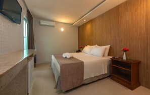 Une chambre d’hôtel moderne équipée d’un lit, d’une table de chevet agrémentée d’un vase de fleurs, d’un téléviseur à écran plat fixé au mur et d’un appareil de climatisation.