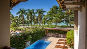 A pool area with lounge chairs, a pergola, and a view of the ocean and palm trees. -  Quinta do Sol Lite Hotel (Porto Seguro)