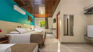 A hotel room with a bed, a wooden headboard, a window with a view of greenery, a mirror, and a bathroom with a sink and towel rack. -  Quinta do Sol Lite Hotel (Porto Seguro)