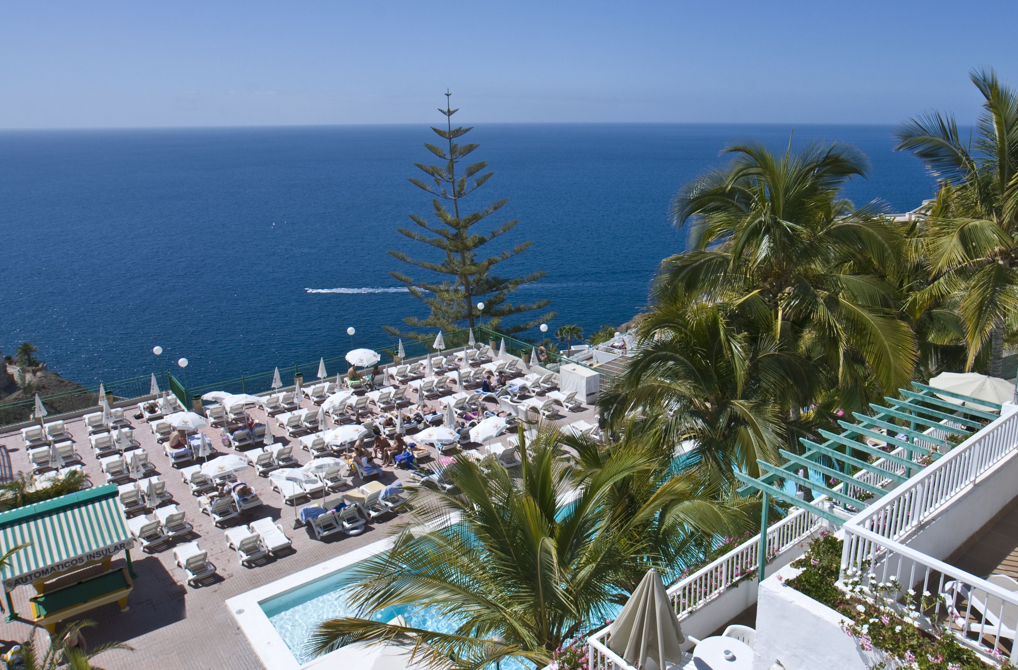 A resort pool area with lounge chairs and umbrellas, overlooking the ocean.