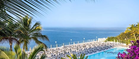 A poolside area with lounge chairs and umbrellas, overlooking a clear blue sea.