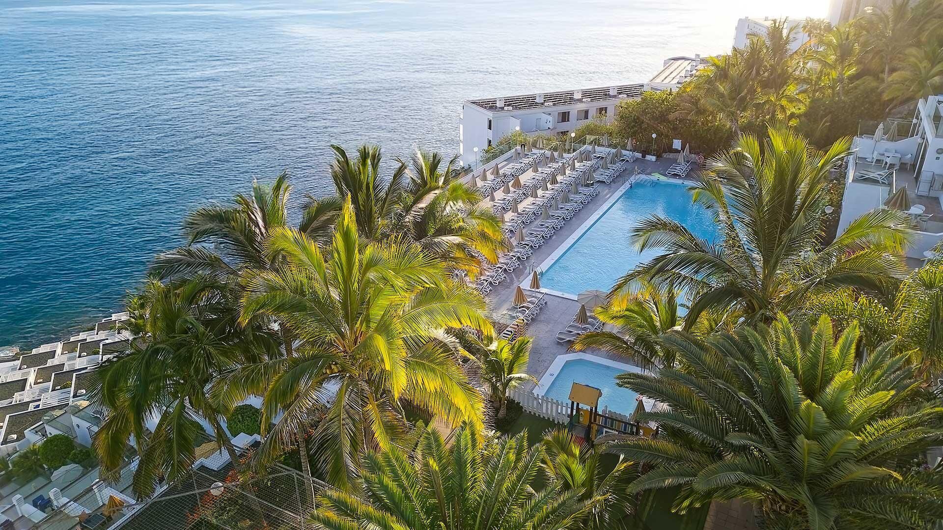 Un resort con piscina, palmeras y vistas al mar.