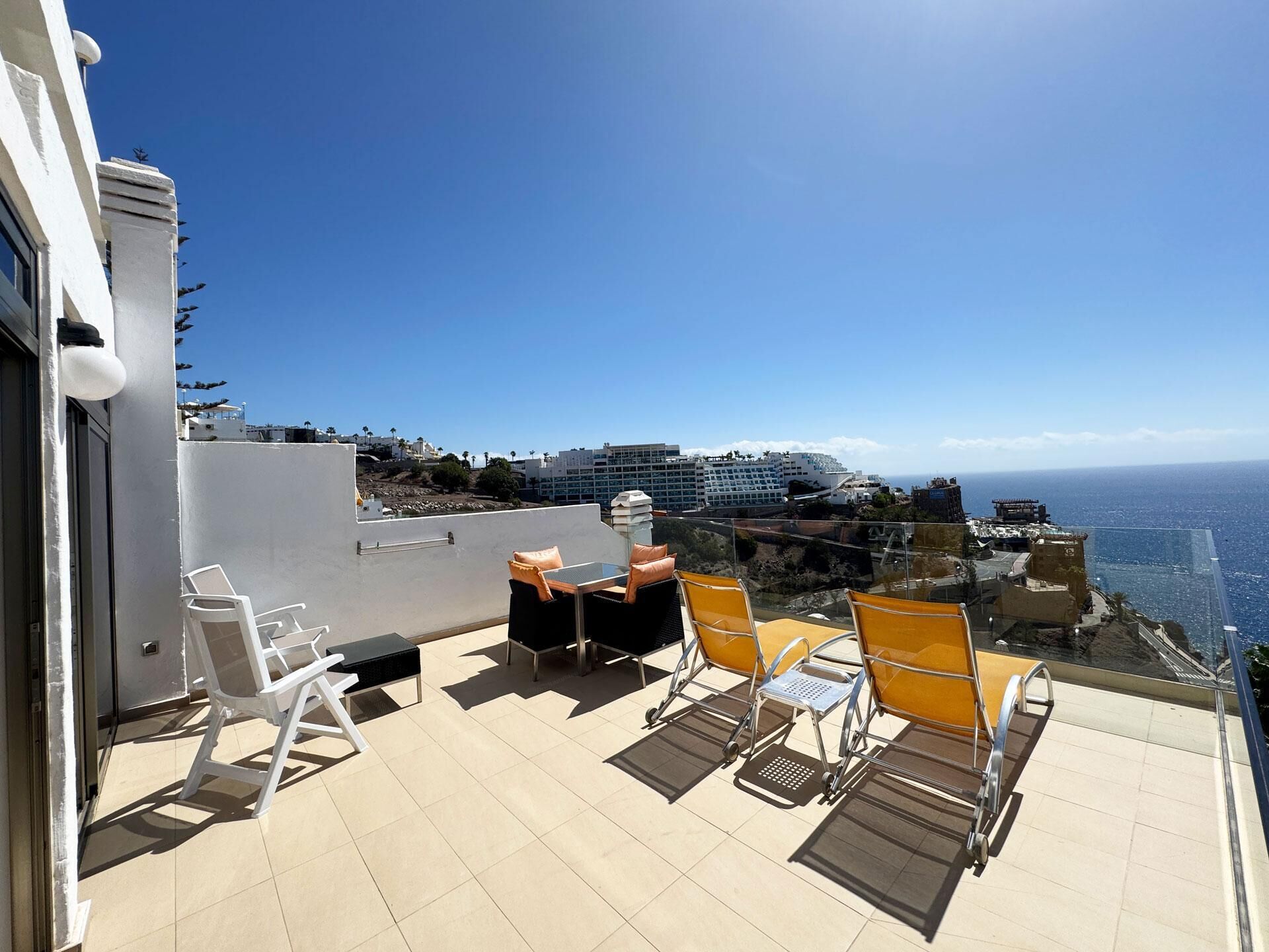 Una terraza en la azotea con mobiliario exterior y vistas al océano y al paisaje urbano.