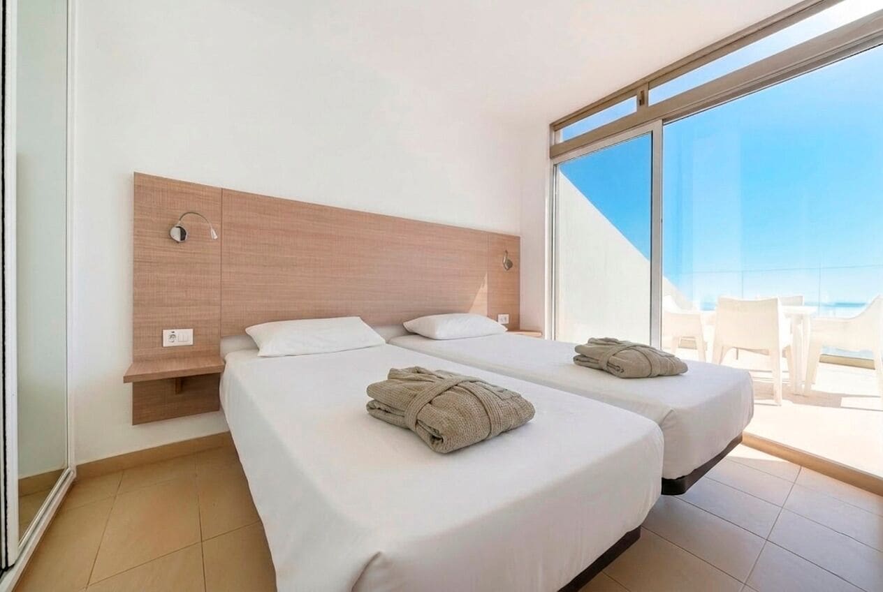 A hotel room with two beds, a wooden headboard, a large window, and a view of the outdoors.