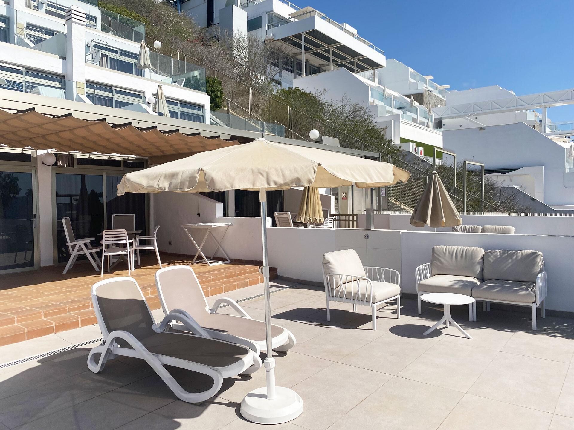 A rooftop terrace with outdoor seating, including lounge chairs and a sofa, under a large umbrella.