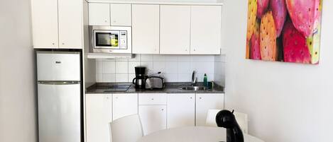 A compact kitchen with white cabinets, a microwave, a coffee maker, and a toaster. There is a round table with chairs and a black hairdryer on it.