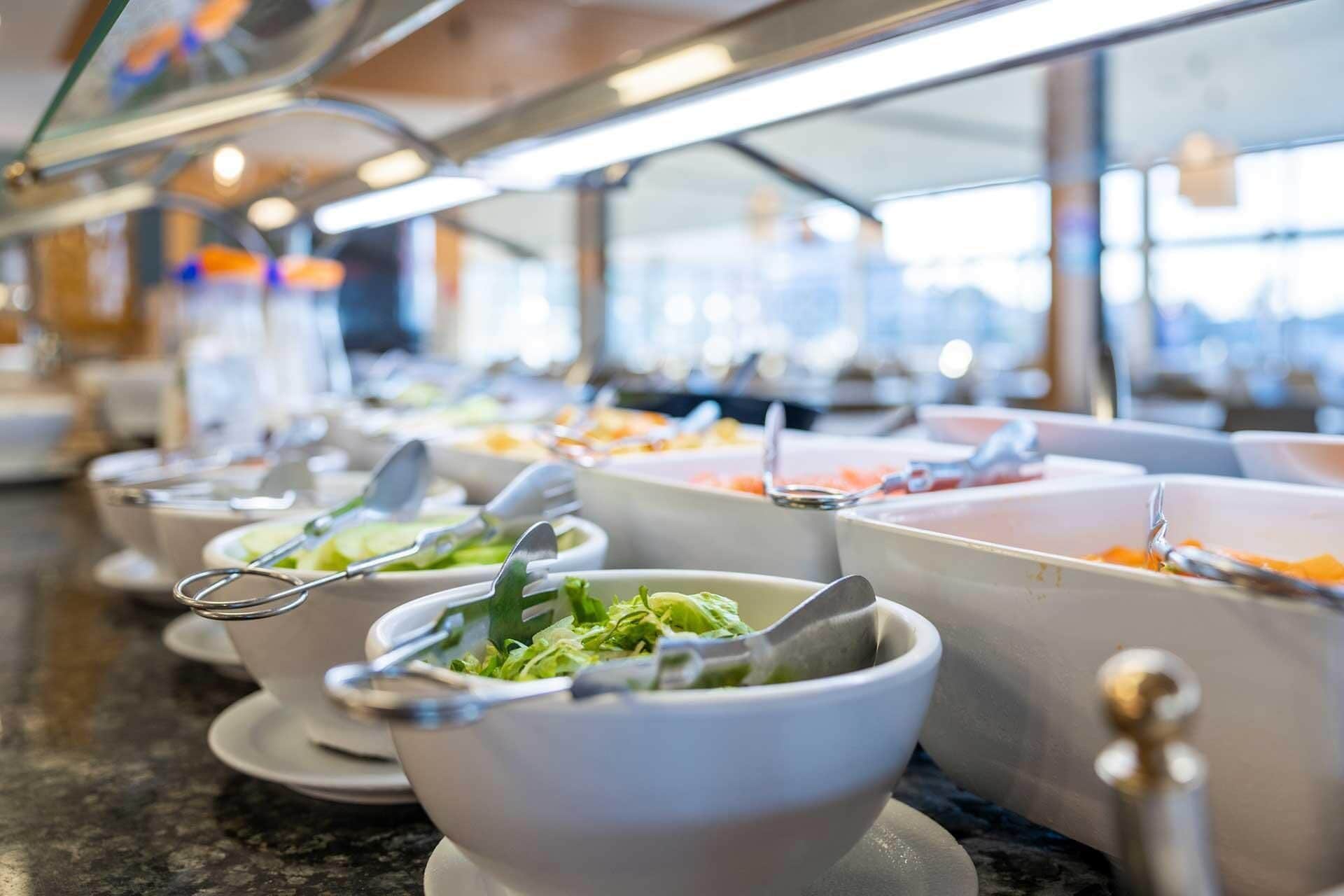 A buffet setup with multiple bowls of food, each with a spoon and a fork.