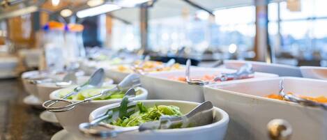 A buffet setup with multiple bowls of food, each with a spoon and a fork.