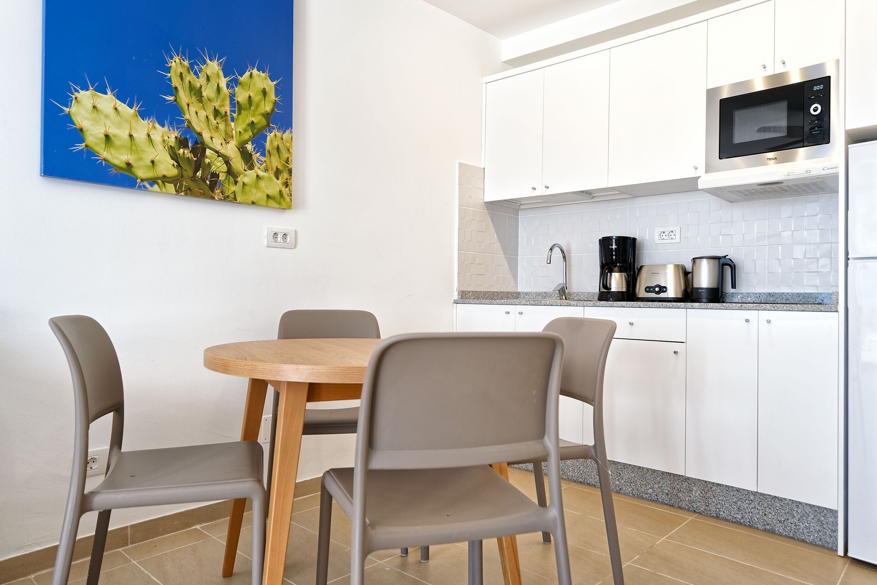 Une cuisine moderne avec des meubles blancs, un four à micro-ondes, une machine à café et un coin repas comprenant une table et des chaises en bois.
