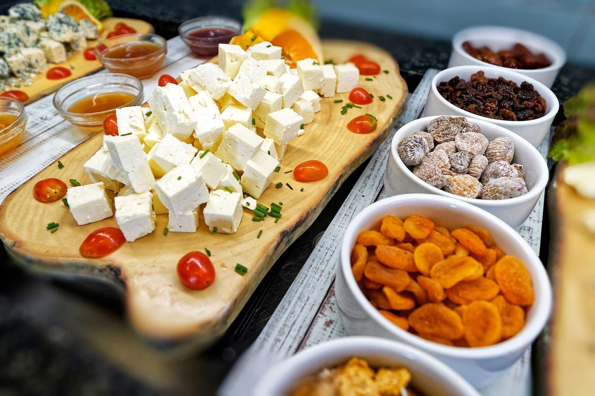 A cheese board with various cheeses, tomatoes, and nuts.