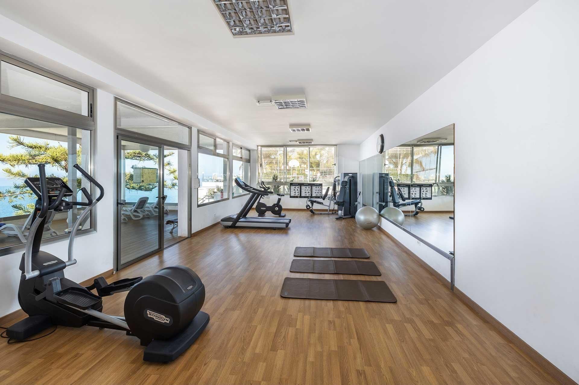 A modern gym with cardio equipment, weight machines, and exercise mats.