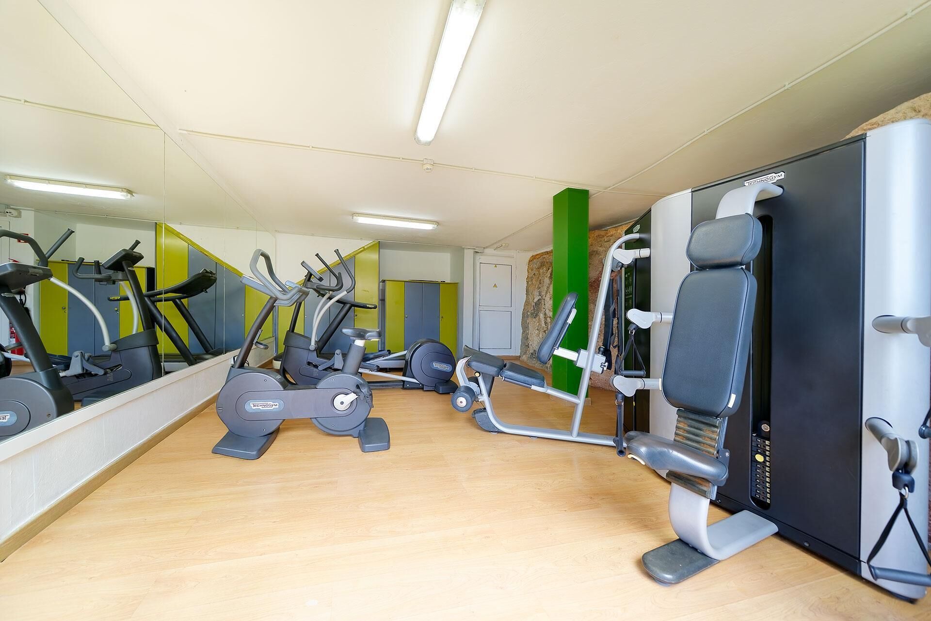 Een sportschool met cardioapparatuur, gewichten en een spiegelwand.