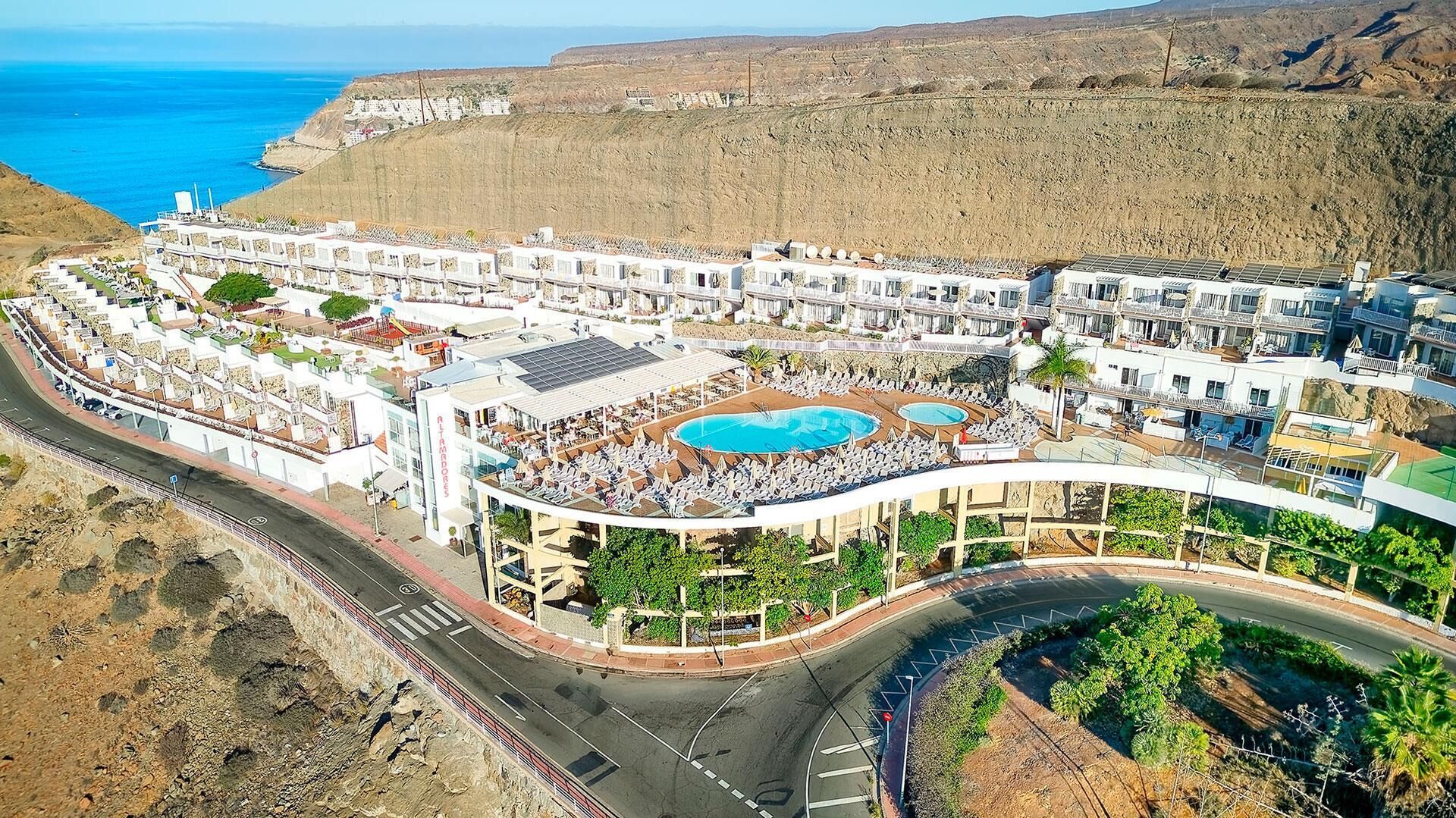 A coastal resort with multiple swimming pools, a road with a roundabout, and a view of the sea.
