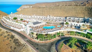 A coastal resort with multiple swimming pools, a road with a roundabout, and a view of the sea. - Servatur Altamadores (Mogan)