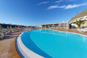 Una amplia piscina al aire libre con tumbonas y sombrillas, una zona de estar cubierta y vistas a la costa.