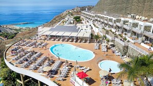 Un resort con una piscina grande, tumbonas y vistas al mar.