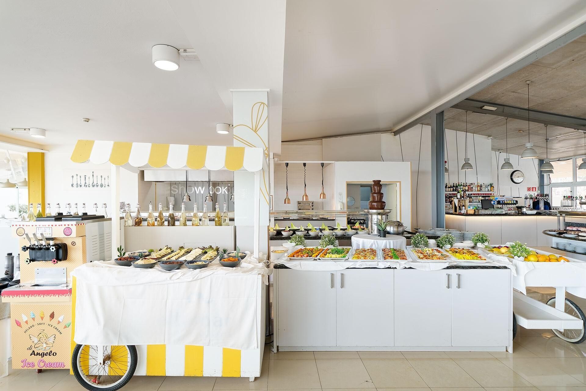Cozinha moderna com serviço de buffet, apresentando diversos tipos de comida e um carrinho de sorvetes.