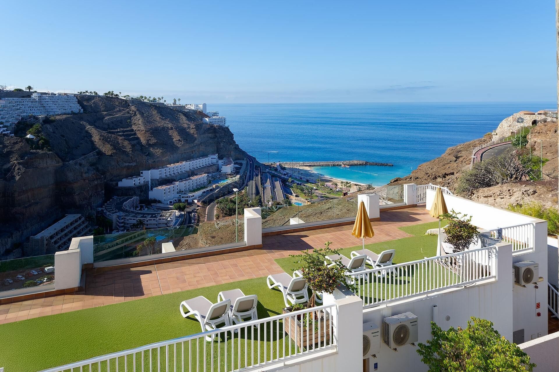 Un hôtel en bord de mer doté d’une terrasse offrant une vue sur l’océan, avec une piscine, des chaises longues et une vue sur la côte rocheuse.