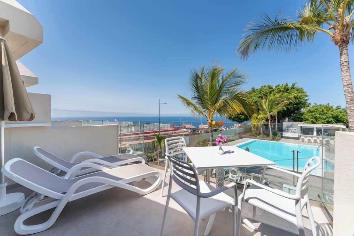 Un balcon avec une piscine, des chaises longues blanches et une table avec des chaises.