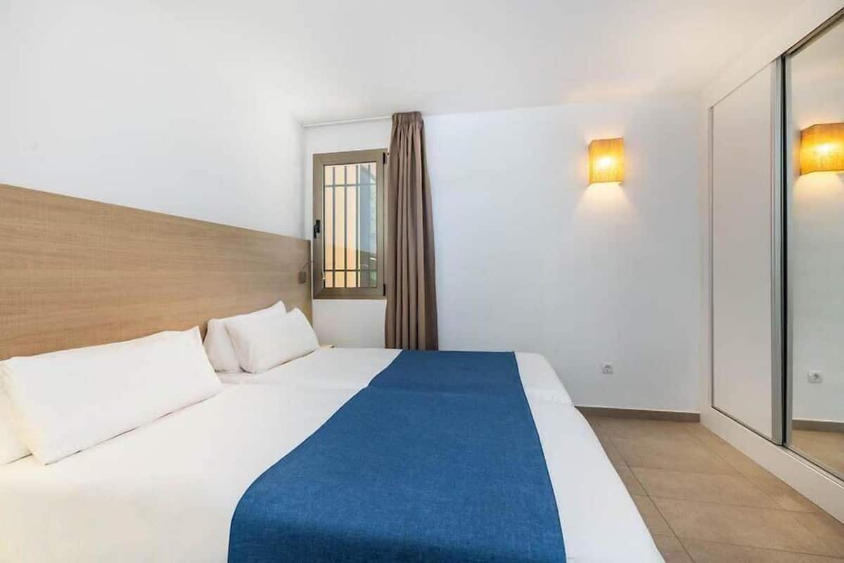 Une chambre d’hôtel avec un lit, une fenêtre avec des rideaux et deux lampes fixées au mur.