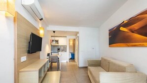 A modern living room with a flat-screen TV, a sofa, a coffee table, and a kitchen area in the background. - Servatur Edén & Buganvillas (Mogan)