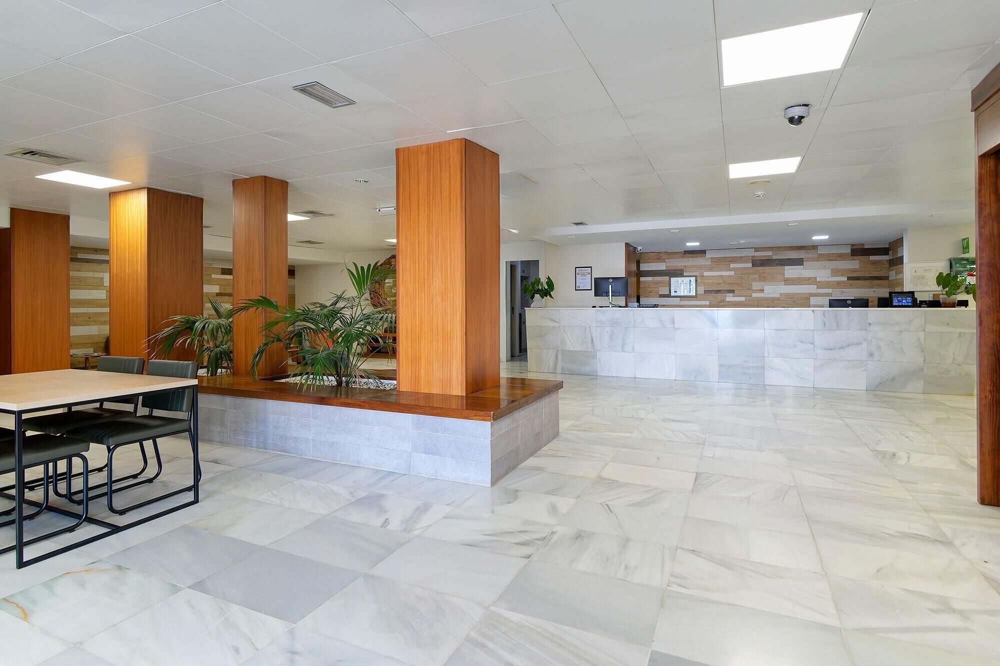 Un'ampia hall con reception, pilastri in legno e un'area salotto con tavolo e sedie.