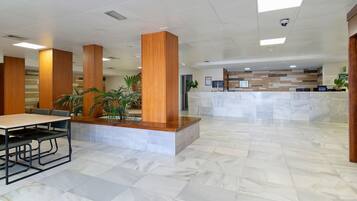Un'ampia hall con reception, pilastri in legno e un'area salotto con tavolo e sedie.