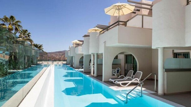 A swimming pool with lounge chairs and umbrellas, surrounded by palm trees and a clear sky. - Servatur Edén & Buganvillas (Mogan)