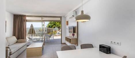 A modern living room with a sofa, a coffee table, a dining table with chairs, a TV, and a ceiling light.