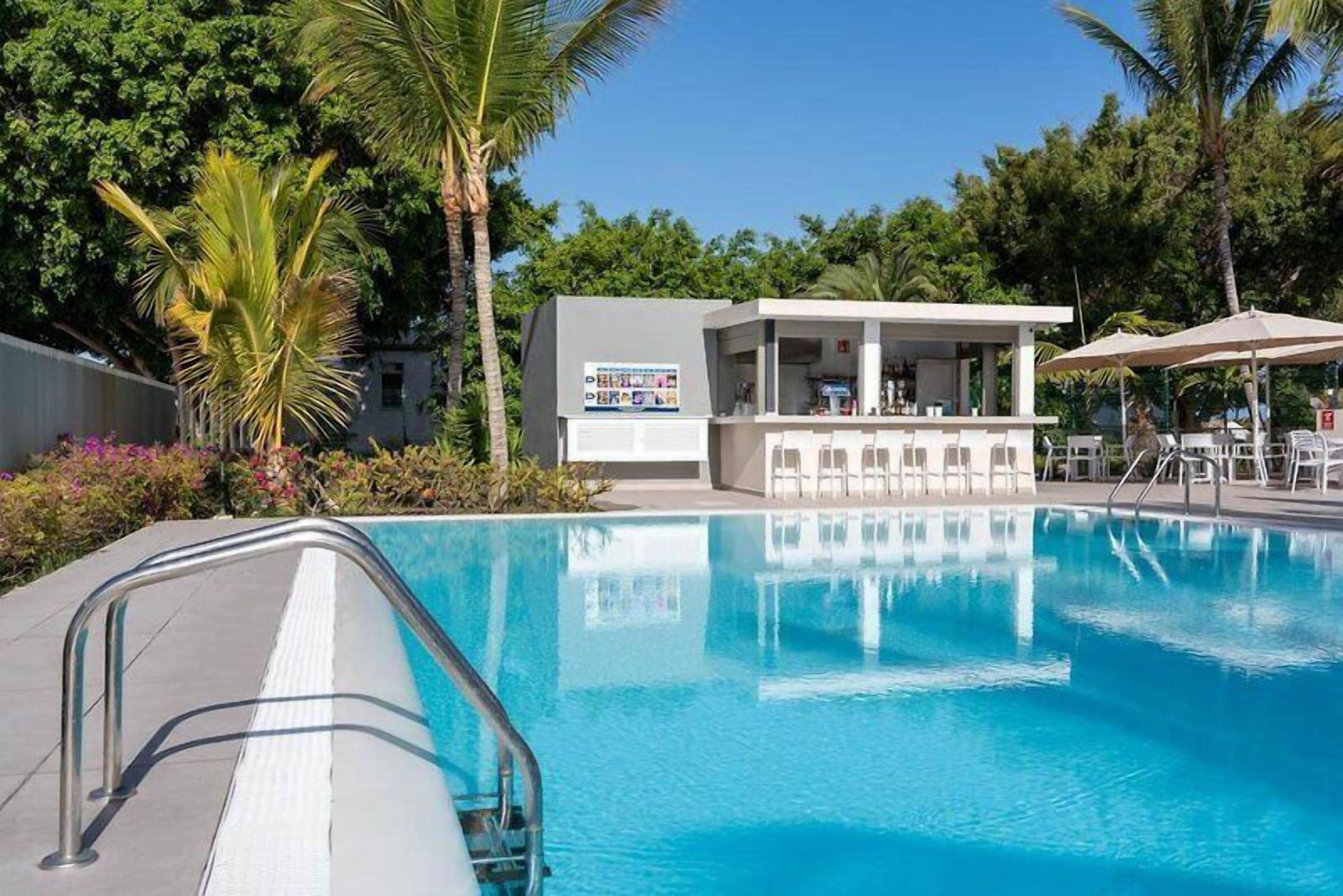 A swimming pool with a bar area, surrounded by palm trees and greenery.