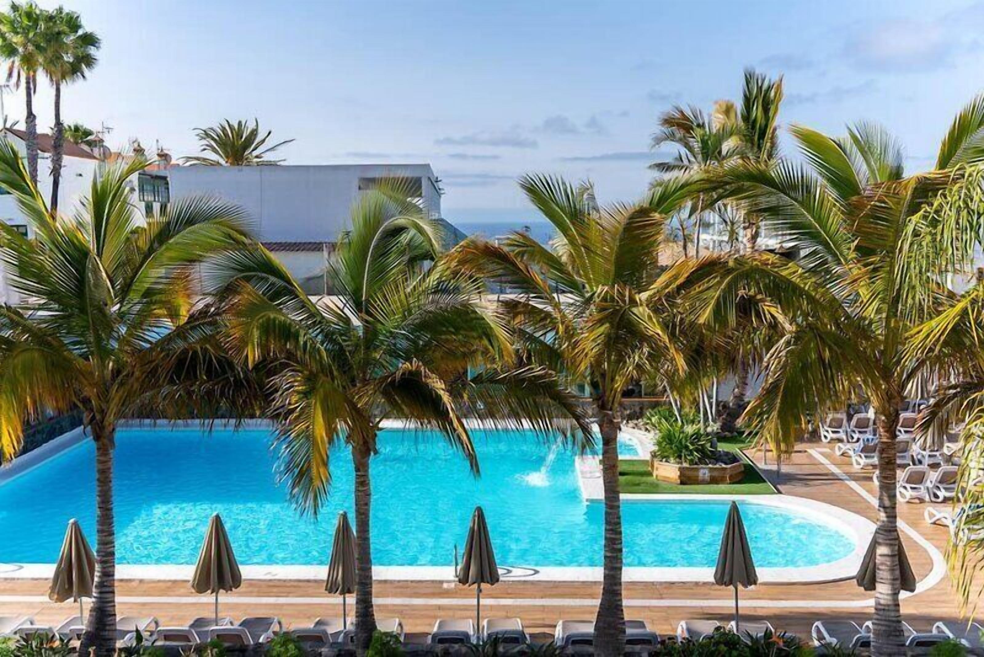 Una piscina al aire libre, sombrillas, sillones reclinables de piscina