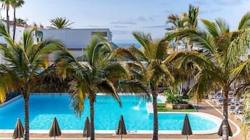 Una piscina al aire libre, sombrillas, sillones reclinables de piscina