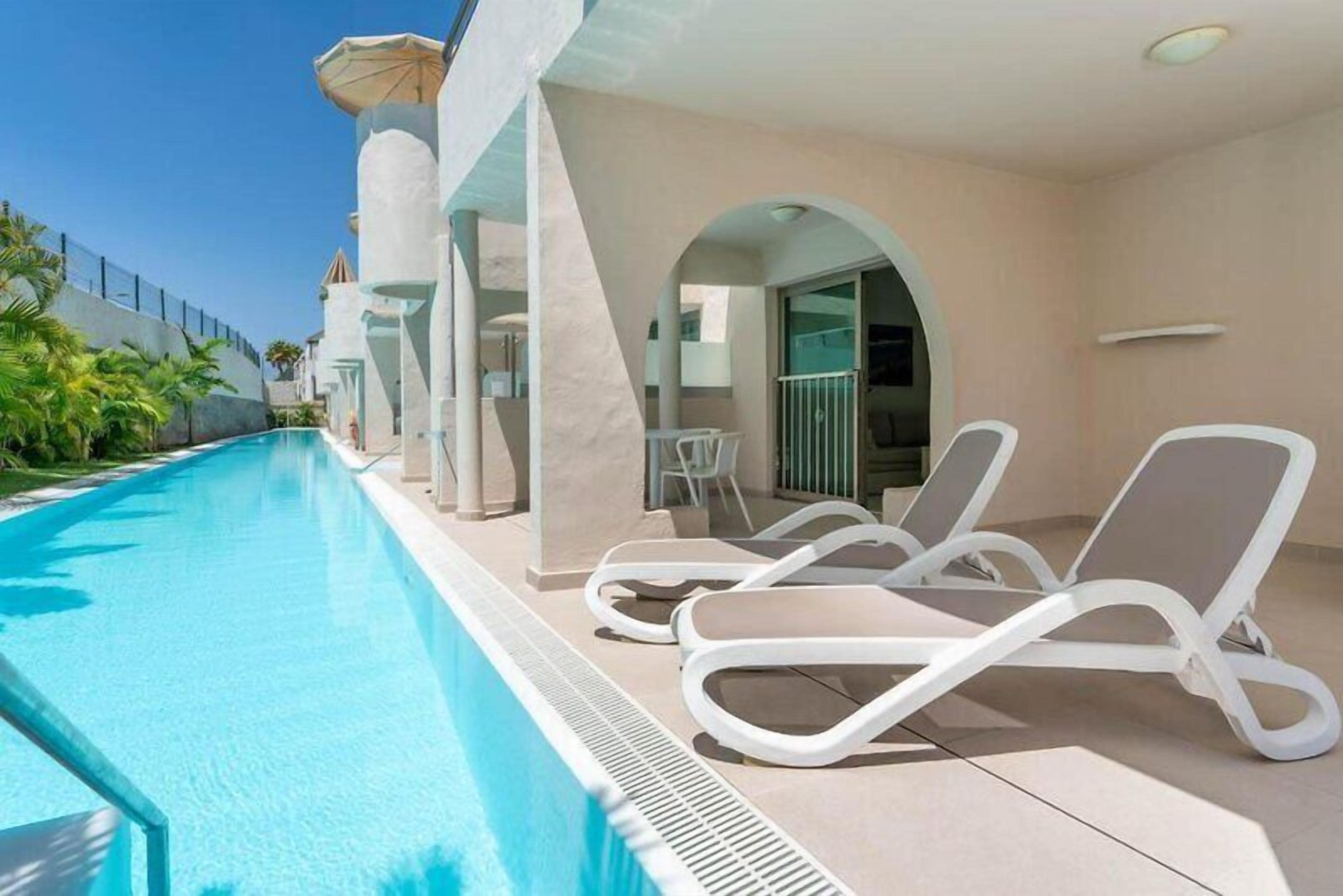 Una piscina con sillones de descanso, una zona cubierta y vistas de los edificios circundantes.