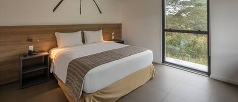 A modern hotel room with a large bed, a wooden headboard, a nightstand, and a large window offering a view of trees.