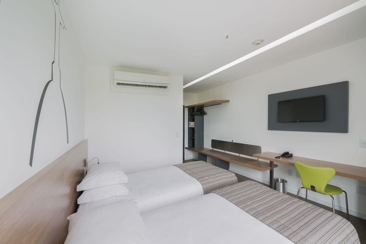 Una habitación de hotel moderna con cama, escritorio, silla, televisor y aire acondicionado.