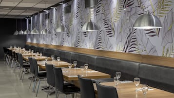 Un restaurante con mesas largas, sillas negras e iluminación colgante.