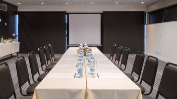 A conference room with a long table, chairs, water bottles, and a projector screen.