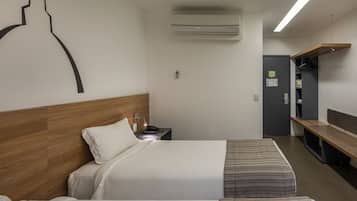 Une chambre d’hôtel avec deux lits, une tête de lit en bois, un bureau avec un téléphone, un appareil de climatisation, un banc et une armoire.