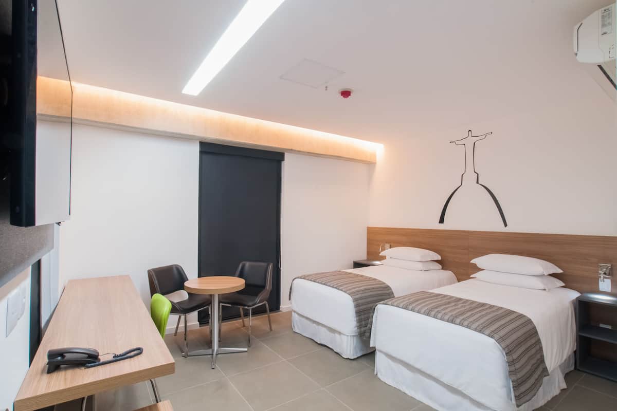 Habitación de hotel con dos camas, un escritorio, un teléfono, una silla y una mesita.