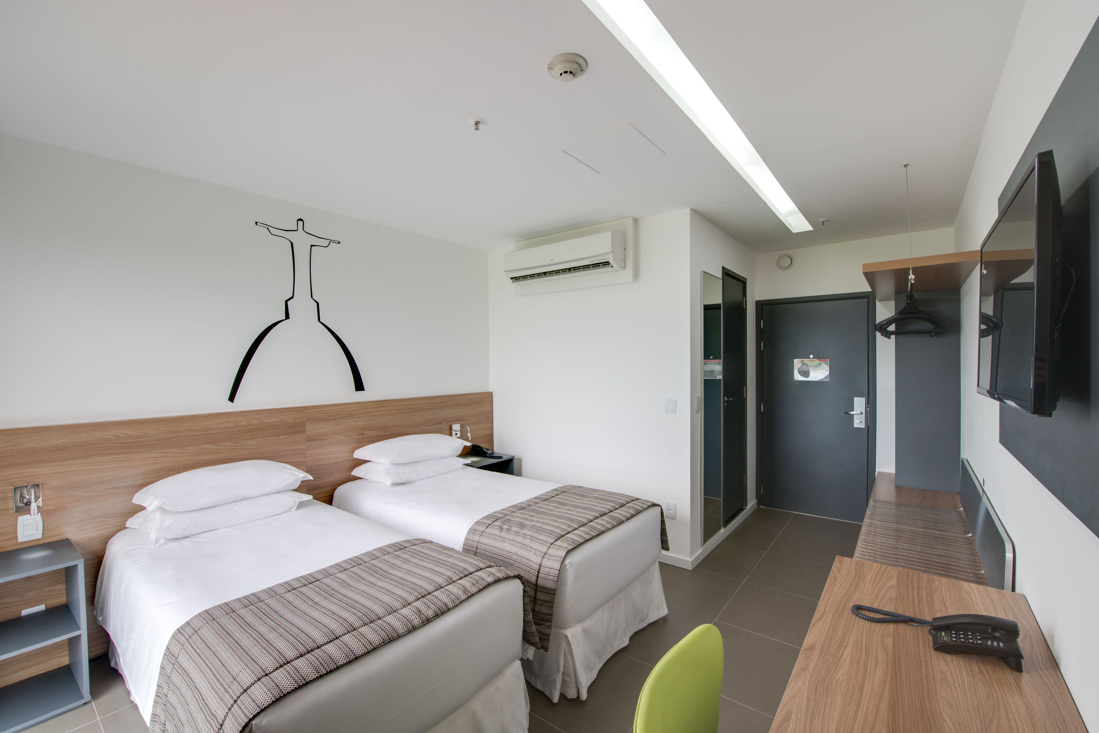 Une chambre d’hôtel avec deux lits, un bureau avec un téléphone, une télévision et un porte-manteau.