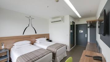 Een hotelkamer met twee bedden, een bureau met telefoon, een televisie en een kapstok.