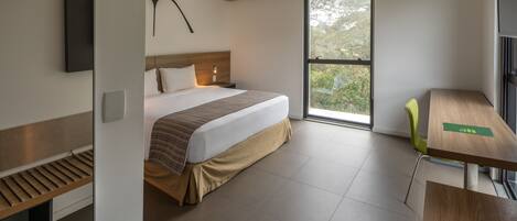 A modern hotel room with a large bed, a desk, and a window with a view of greenery.